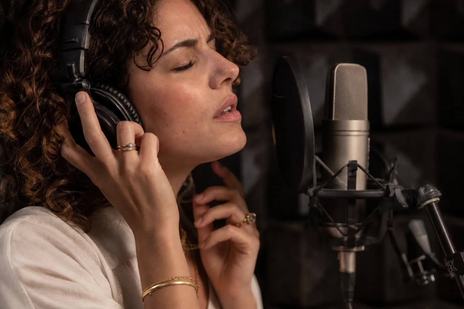זמרת מקליטה שירה בעברית מול מיקרופון אולפני עם פופ פילטר בתא אקוסטי