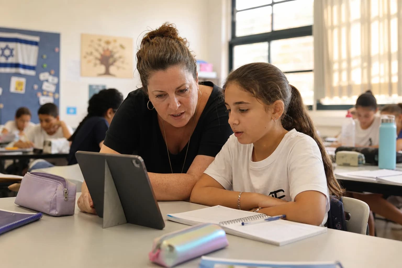 מורה ותלמיד מביטים יחד בטאבלט בכיתה בבית ספר ישראלי