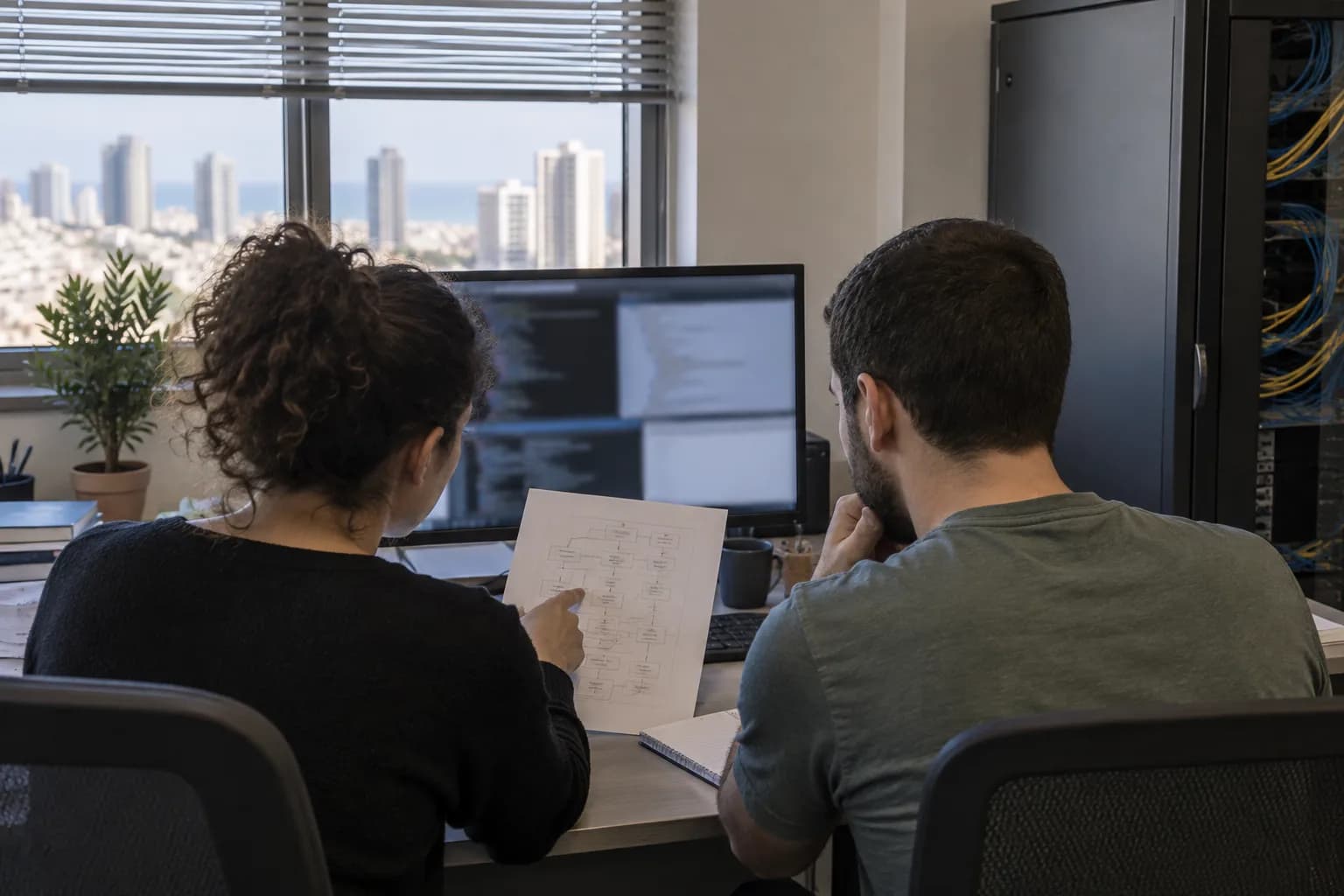 המחשה של צוות בדיקת אבטחת תוכנה במשרד בישראל מול מסך ותרשים טכני