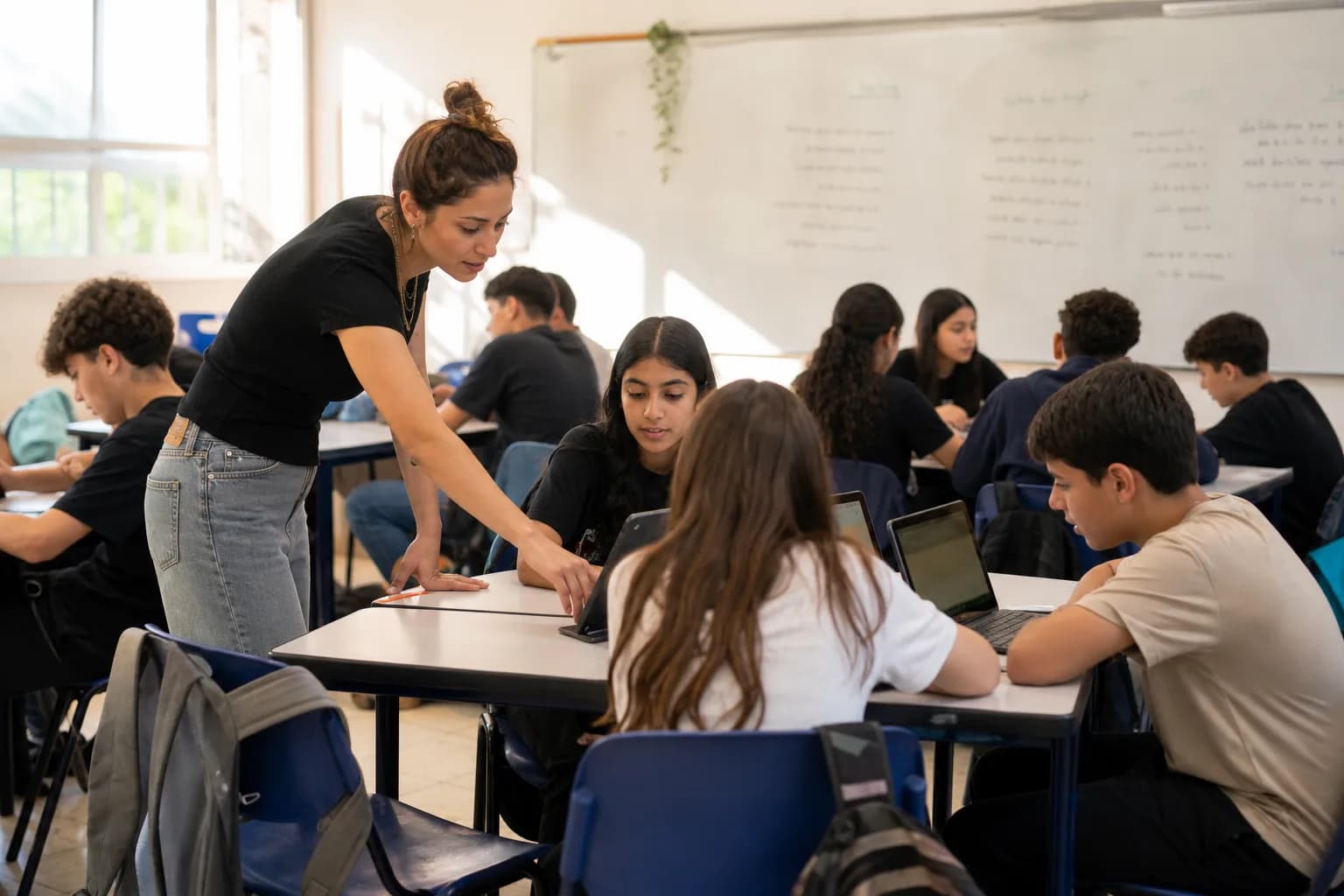 תלמידים בכיתה בבית ספר בישראל עובדים על מחשבים ניידים בליווי מורה