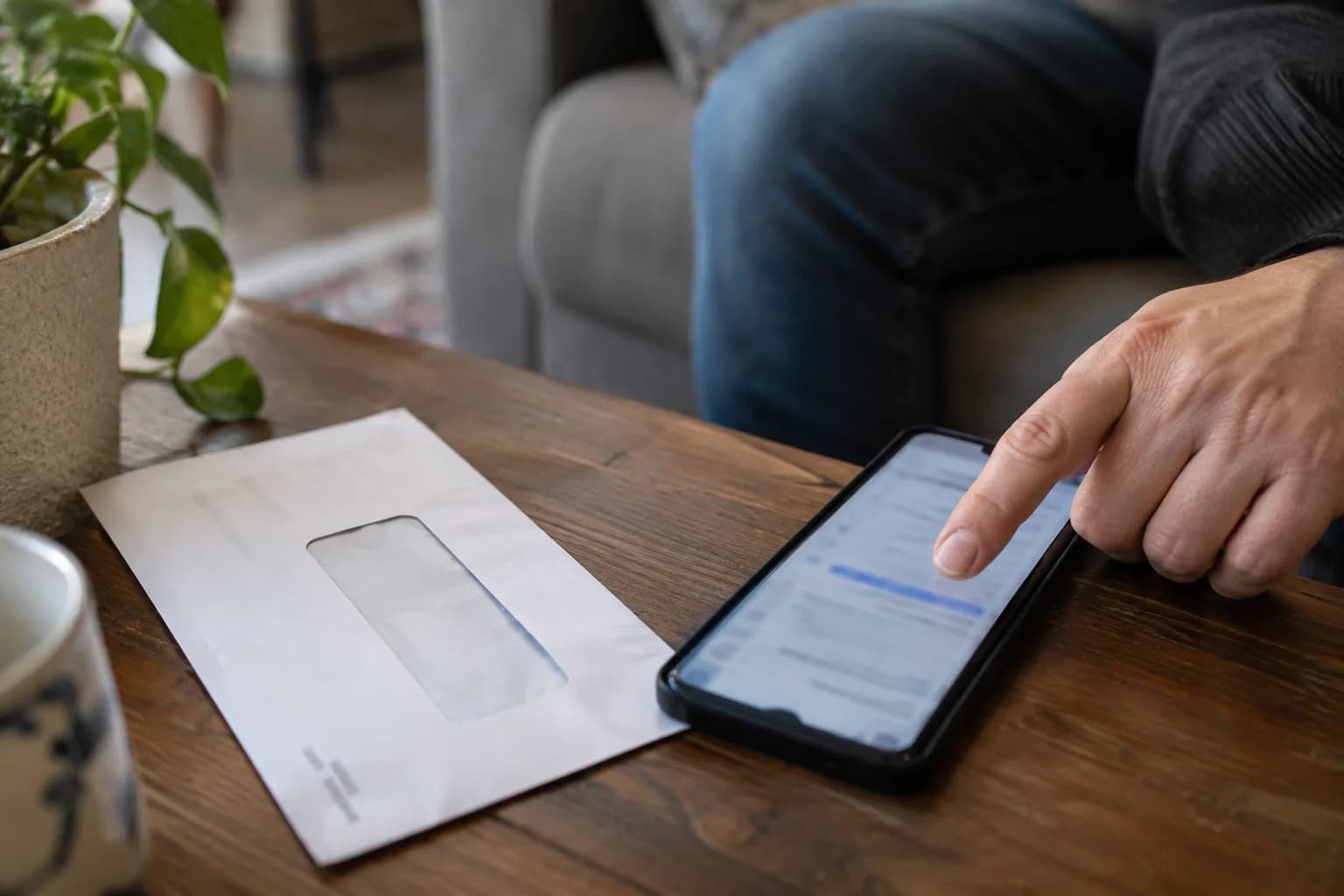 טלפון מונח לצד מעטפת חשבון על שולחן ביתי, ואצבע מצביעה על כתובת קישור מטושטשת במסך