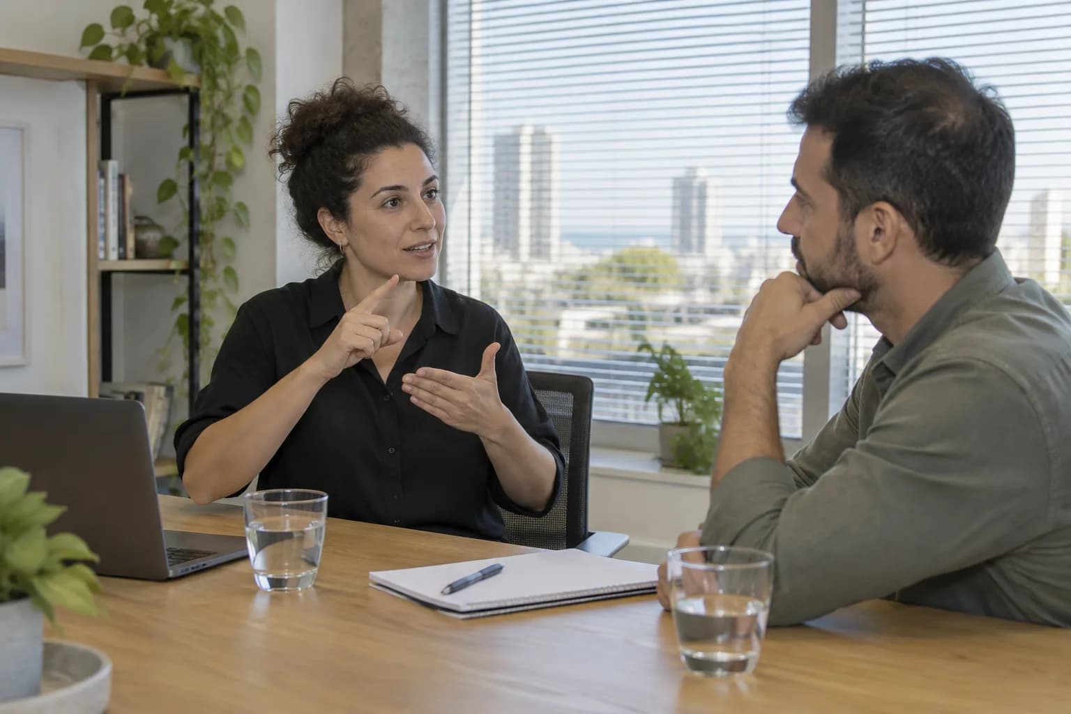 עובד מתקשר בשפת סימנים עם עמיתה בחדר ישיבות, לצד מחשב נייד פתוח