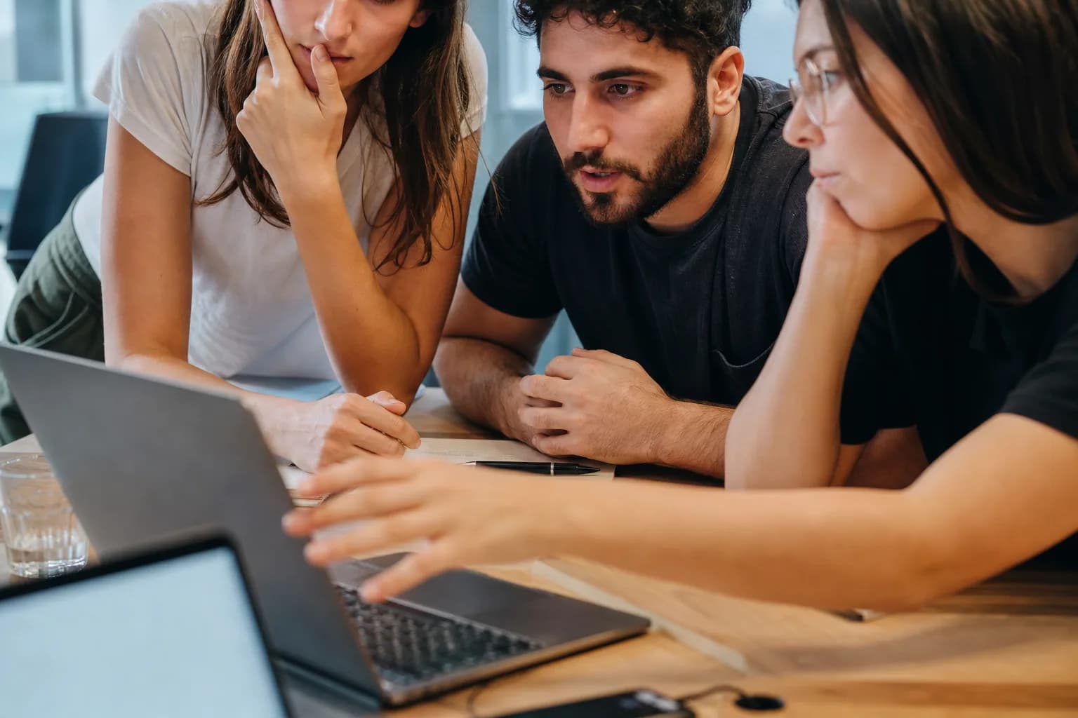 צוות פיתוח צעיר יושב סביב שולחן עבודה פתוח במשרדי סטארטאפ בתל אביב ומסתכל יחד על מסך